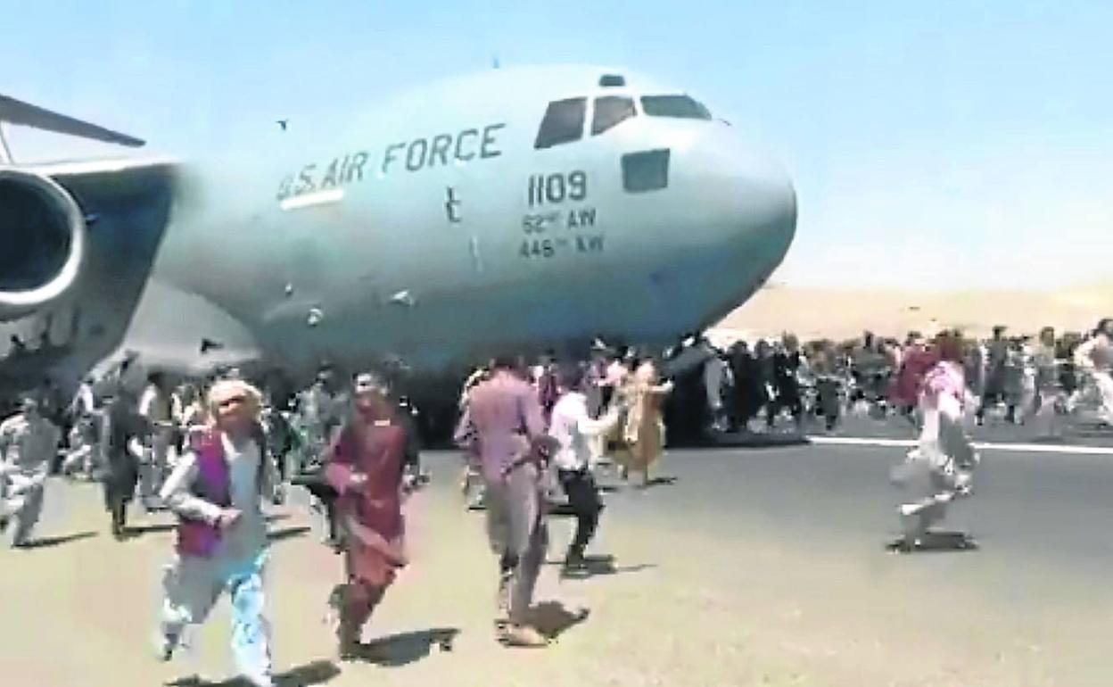 Cientos de afganos intentan impedir el despegue de un avión militar estadounidense en el aeropuerto de Kabul, hace ya un año.