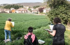 Tres de las pintoras, en un campo reflejando una vista del pueblo.