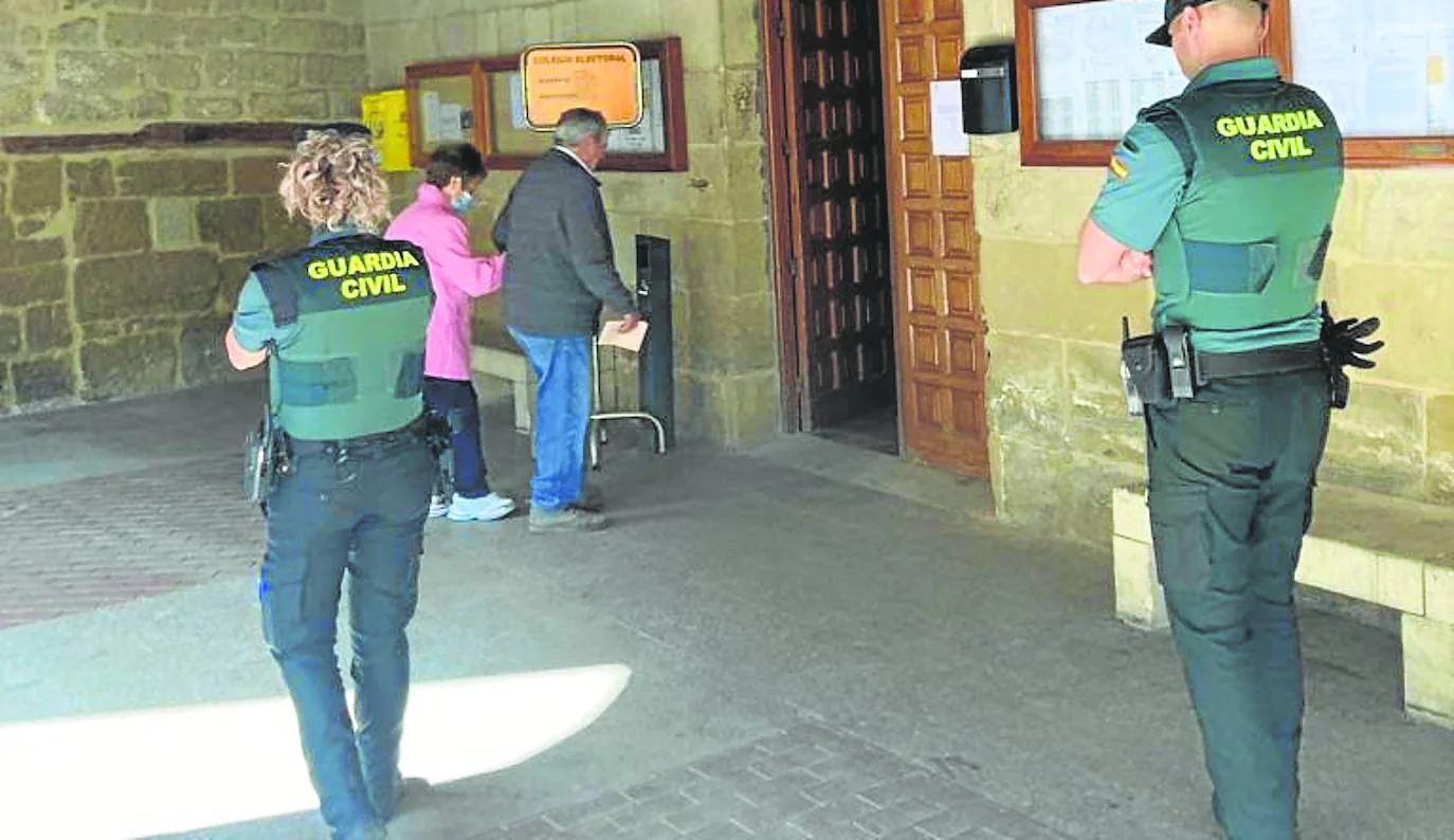 Dos personas acuden a votar al Ayuntamiento de San Asensio este domingo, ante la mirada de dos agentes de la Guardia Civil.
