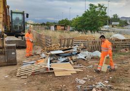 Dos operarios retiran palés y otros restos que conforman las improvisadas huertas.