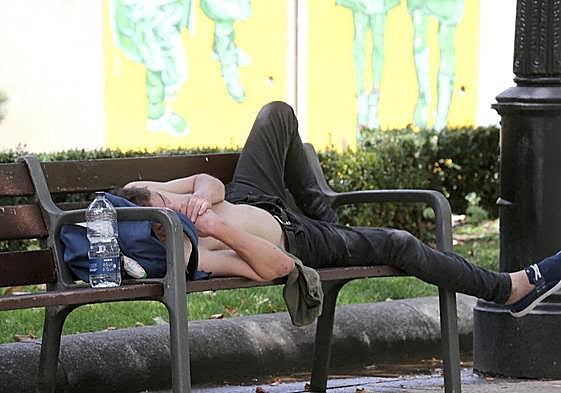 Un joven se tumba descamisado y con la botella de agua al lado, en un parque de Logroño.