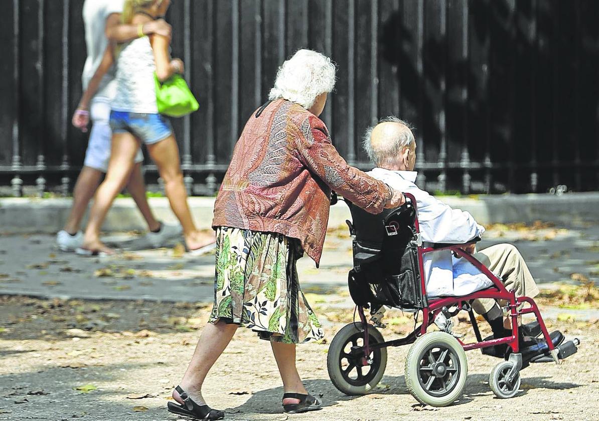 Una anciana empuja la silla de ruedas de su marido.