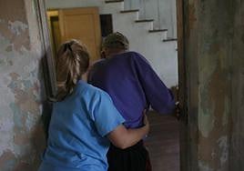 Un anciano es ayudado a desplazarse por una enfermera.