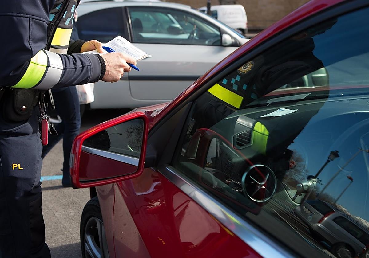 Un agente de la Policía Local, boletín de sanciones en mano, denuncia a un vehículo mal estacionado en una imagen de archivo.