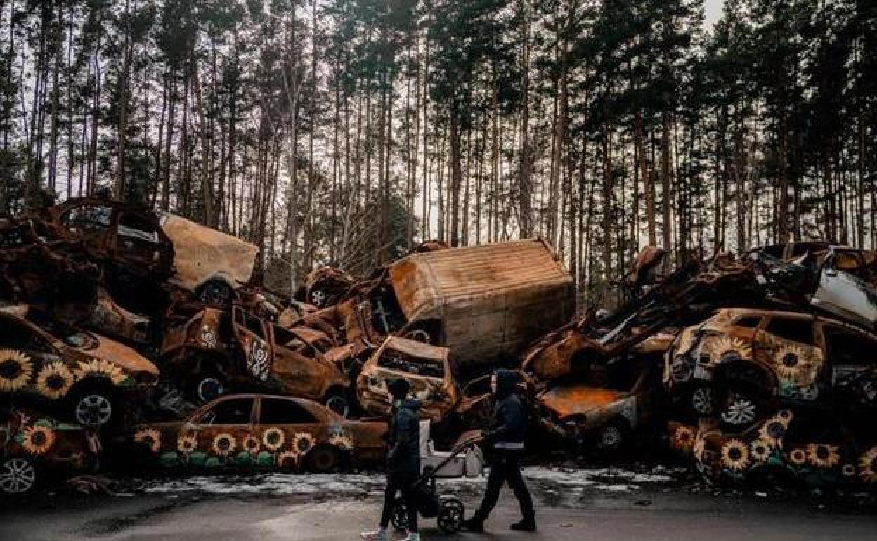 Una pareja y su hijo pasan frente a un cementerio de vehículos destruidos en la batalla de Irpin.