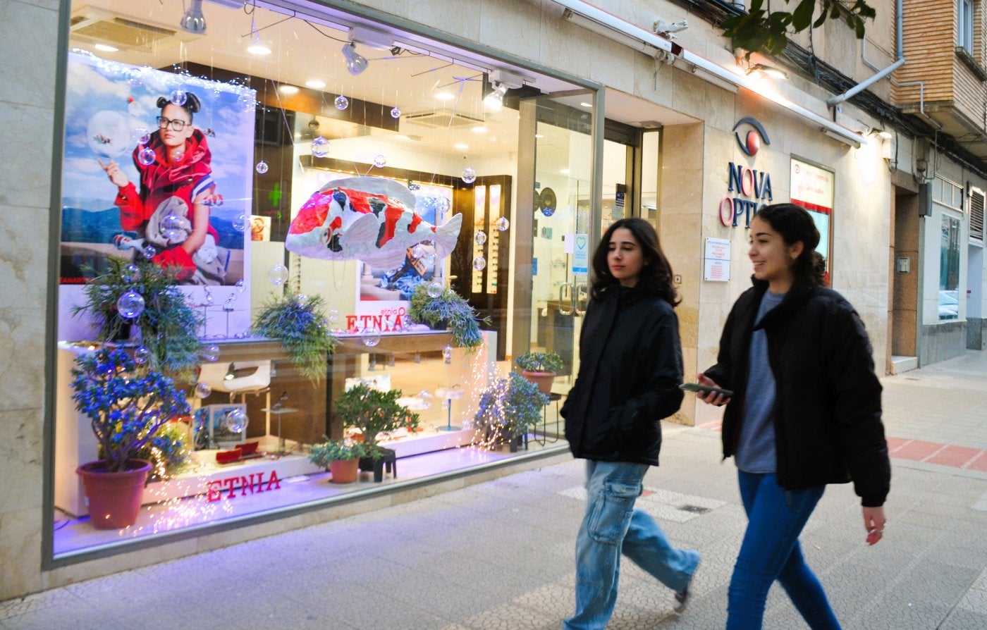 Dos jóvenes pasan por delante de un original escaparate navideño, en una óptica de Achútegui de Blas.
