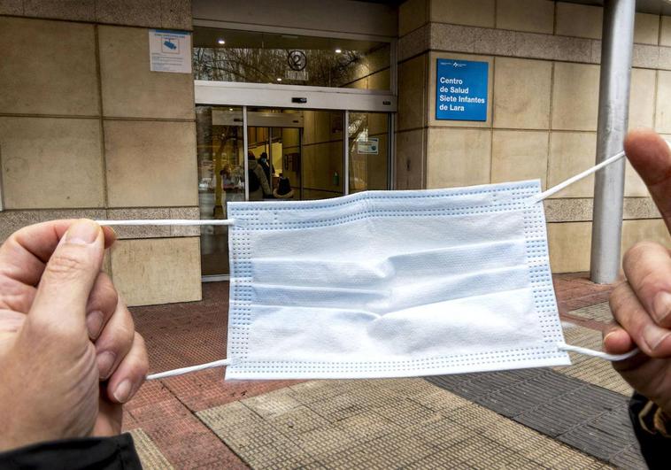 Un paciente se dispone a colocarse la mascarilla junto al centro de salud Siete Infantes de Lara.