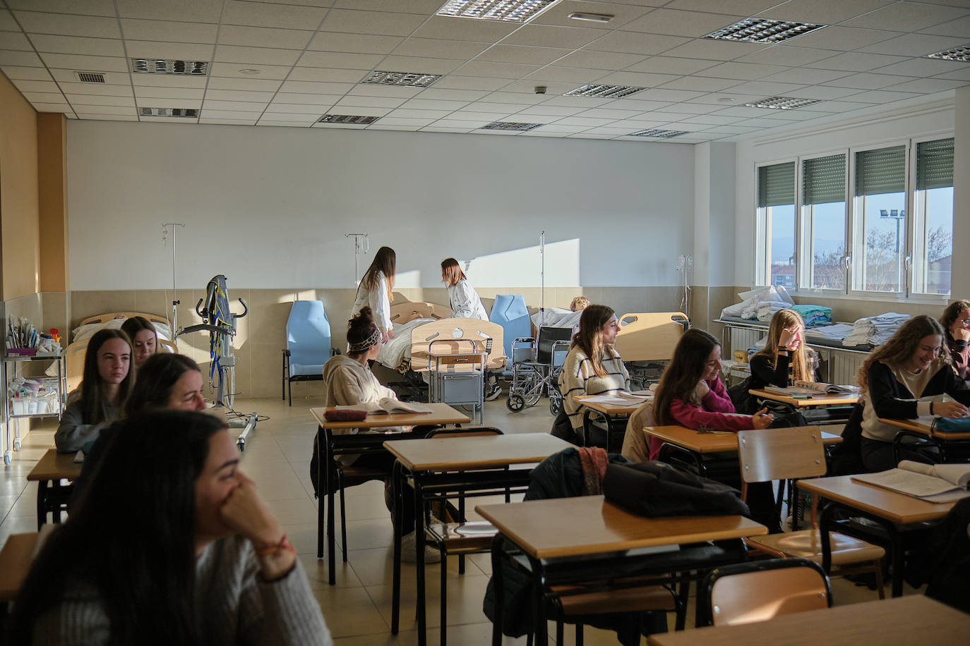 Dos estudiantes del grado medio de Cuidados Auxiliares de Enfermería hacen prácticas con un muñeco mientras sus compañeros atienden a su profesora.