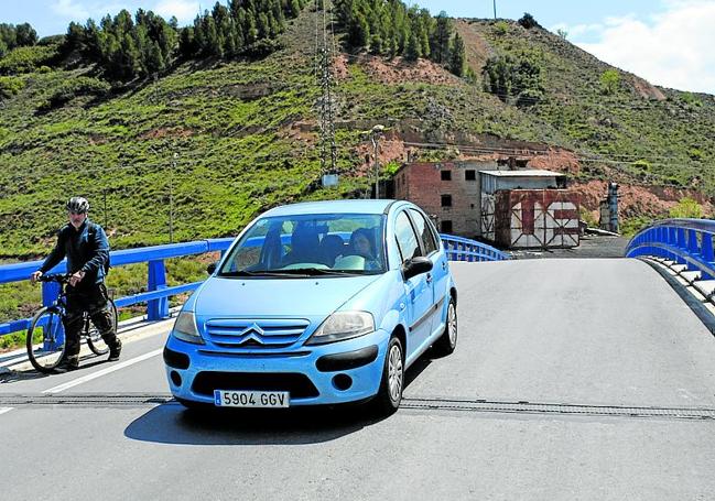 Un coche rebasa a un hombre que camina con su bici sobre el puente