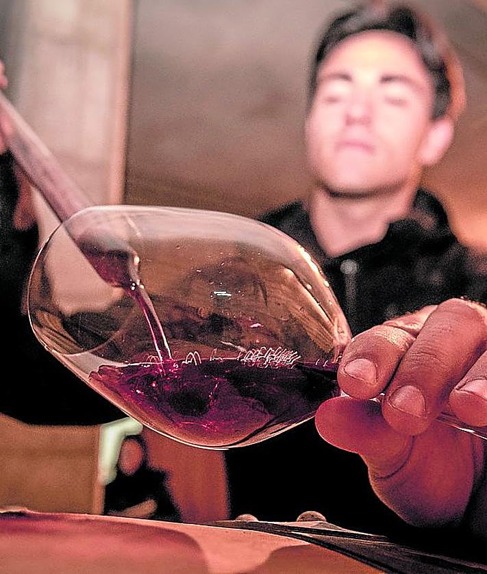 Imagen secundaria 2 - Arriba, Isabel en la zona de botellas. Abajo, David atiende una visita guiada y echa vino a una copa.