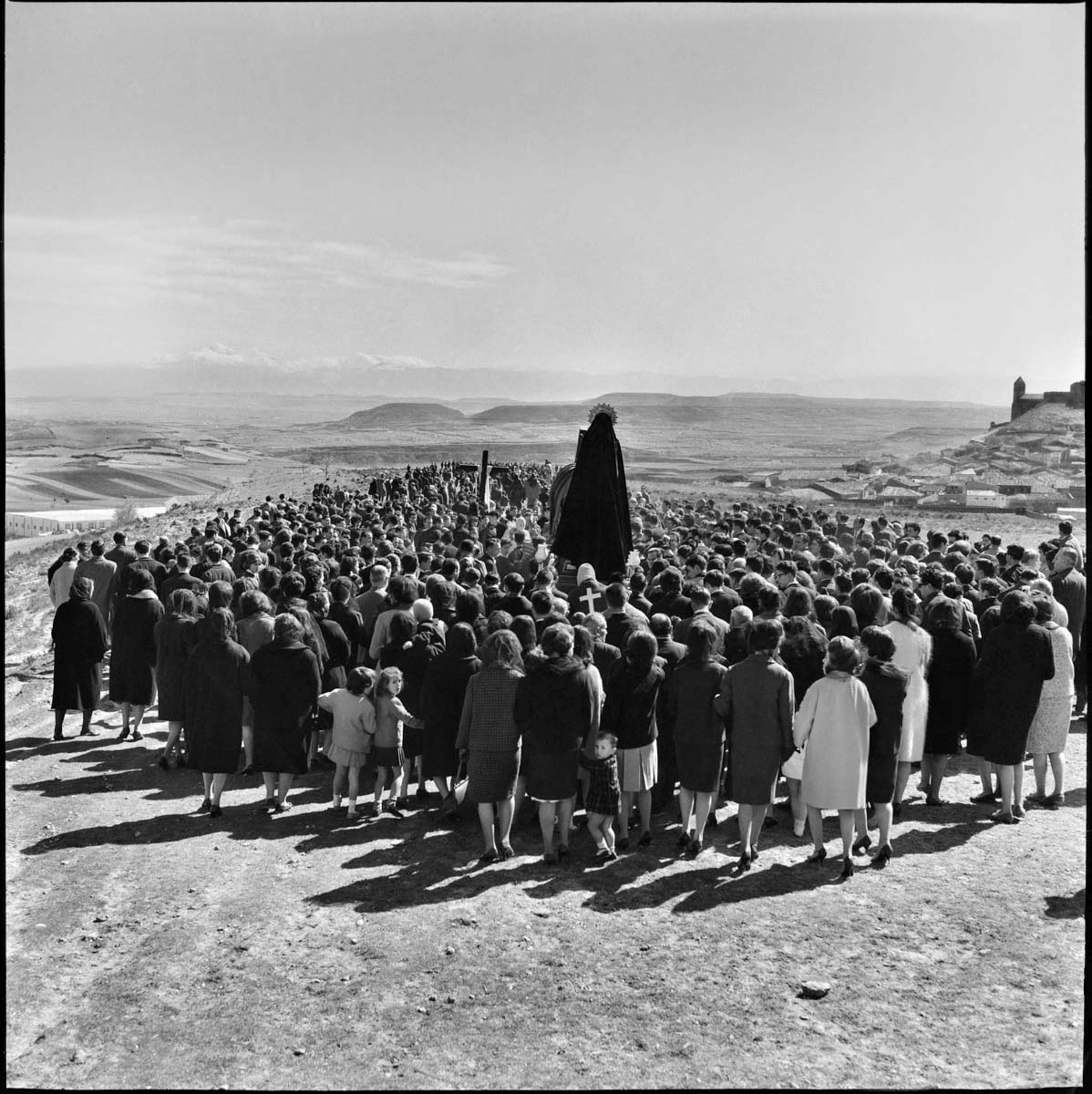 Cuando Teo se dirigía a realizar los encargos para 'La Gaceta del Norte' siempre llevaba dos cámaras: la de 35 mm. para los reportajes y la Rolleiflex, de formato cuadrado, para sus fotografías. Aquí se levanta sobre la masa negra de la procesión, con unos penitentes que apenas se adivinan entre la multitud, y encaramado a una cruz del Vía Crucis y sus casi dos metros de altura espera a que todos se olviden del fotógrafo y se sumerjan en el rito, en la fe, en el acompañamiento. Todos, menos la niña que se vuelve, y el fotógrafo, avispado, presiona el disparador.