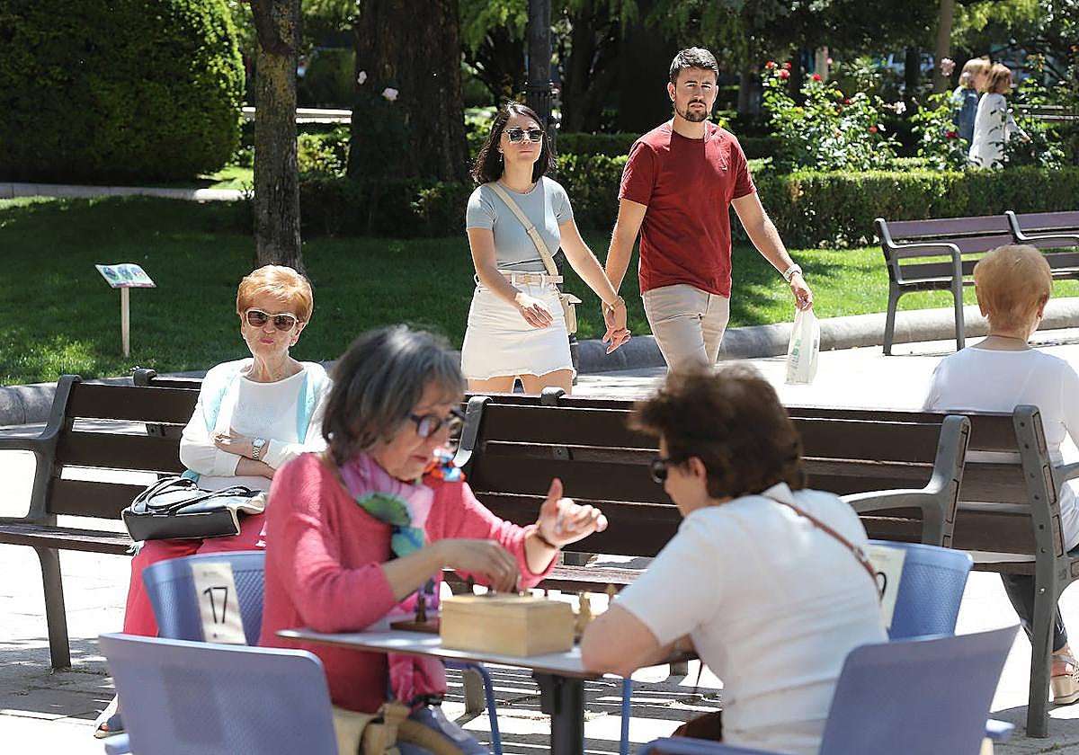Una pareja pasea por El Espolón mientras dos mujeres juegan al ajedrez.