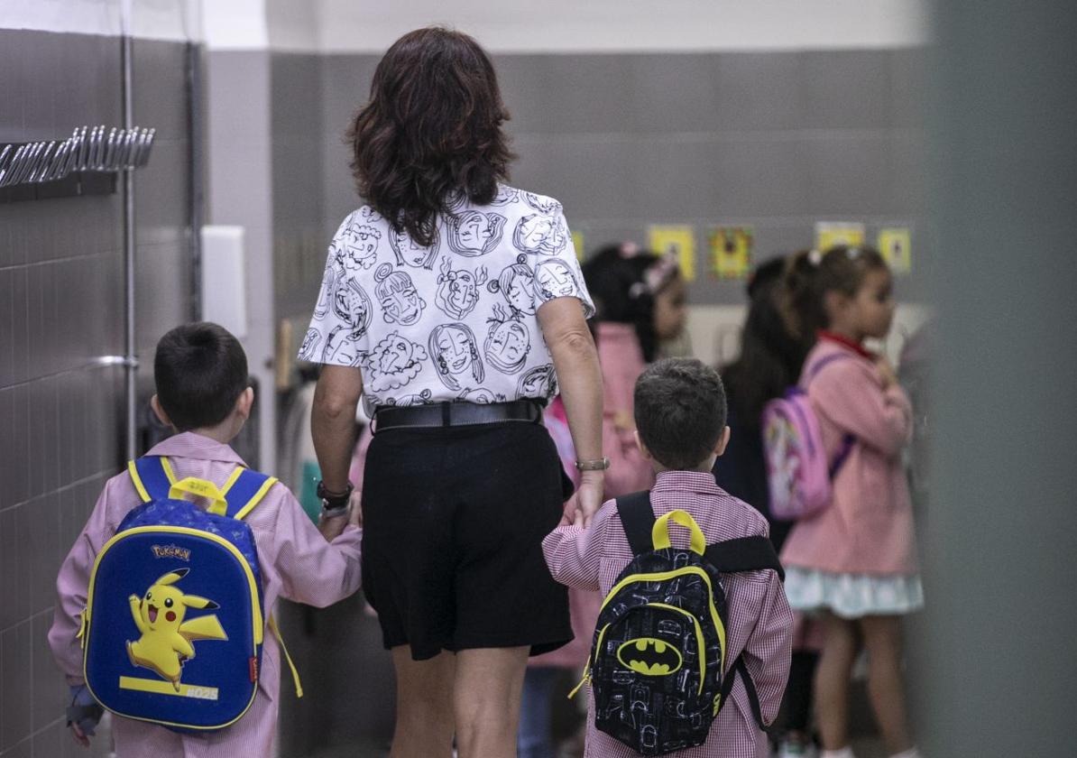 Una profesora lleva a dos niños a clase en el inicio del curso escolar.