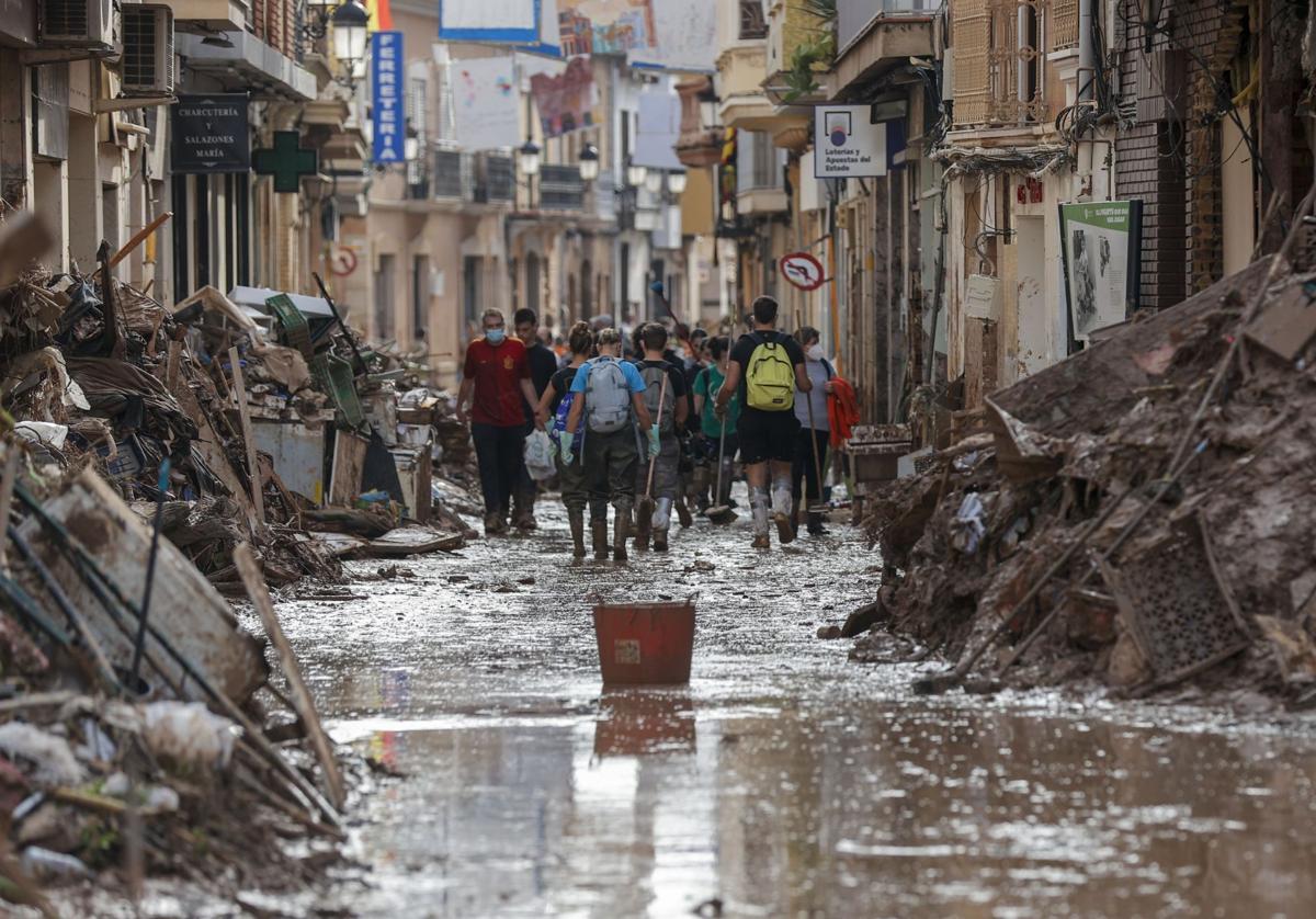 Voluntarios y afectados por la DANA, en una calle de Paiporta.