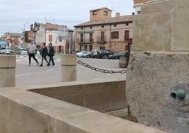 Varios vecinos caminan al fondo, con la fuente de la plaza de la Constitución, seca en primer plano.