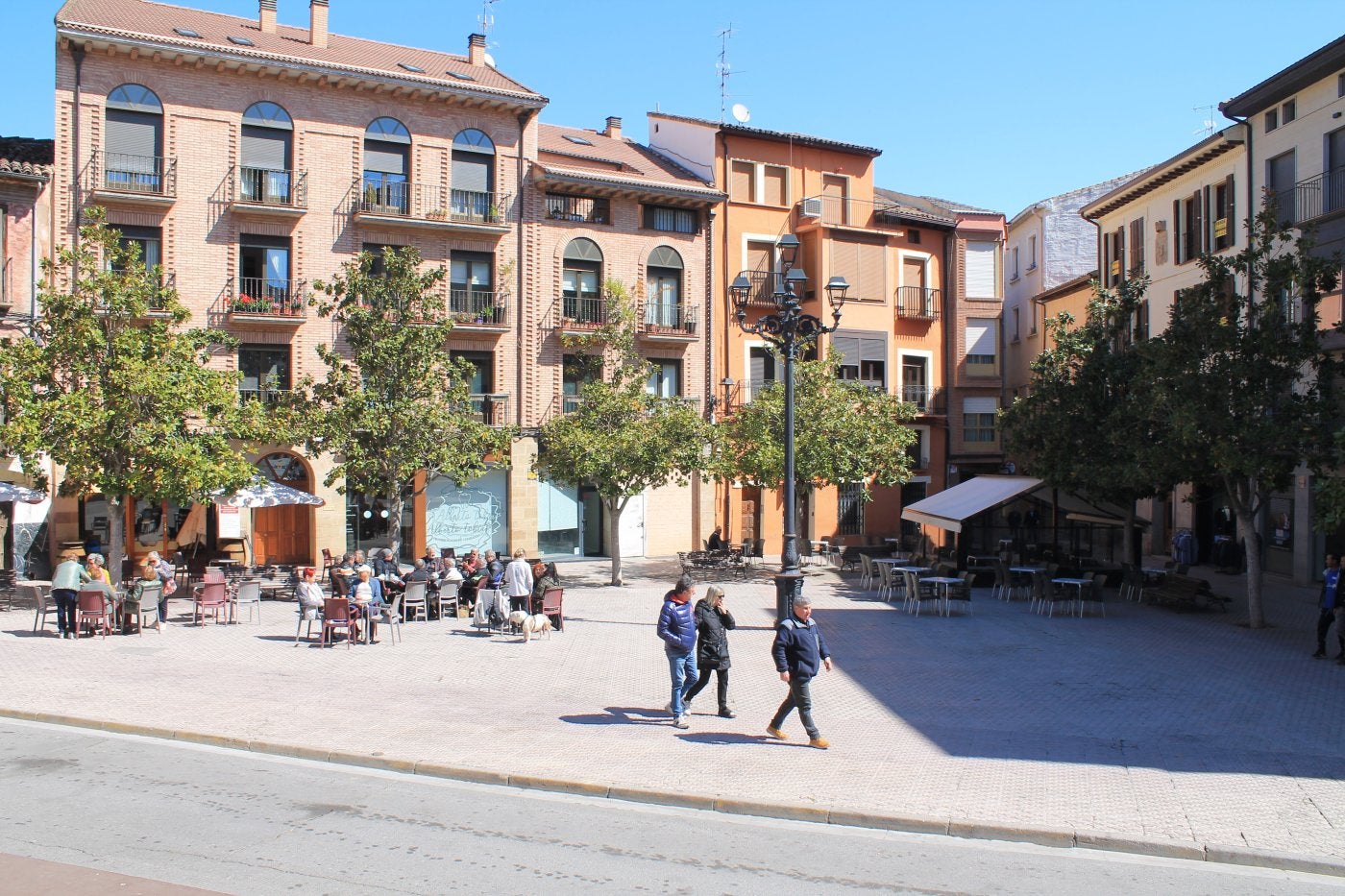 Tres personas pasean por la emblemática plaza de España de Nájera, mientras otras toman algo en las terrazas, durante una mañana soleada.