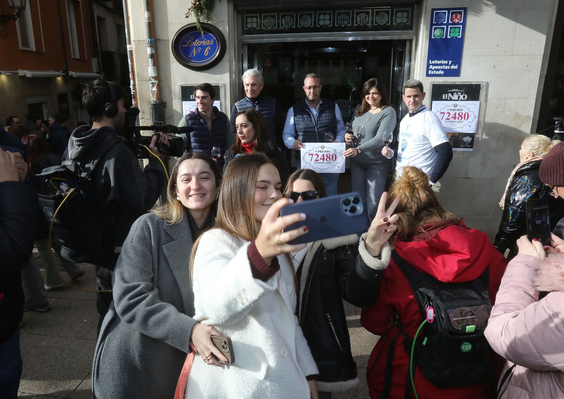 Unas jóvenes se hacen un selfi con los loteros que han vendido el primer premio, al fondo.