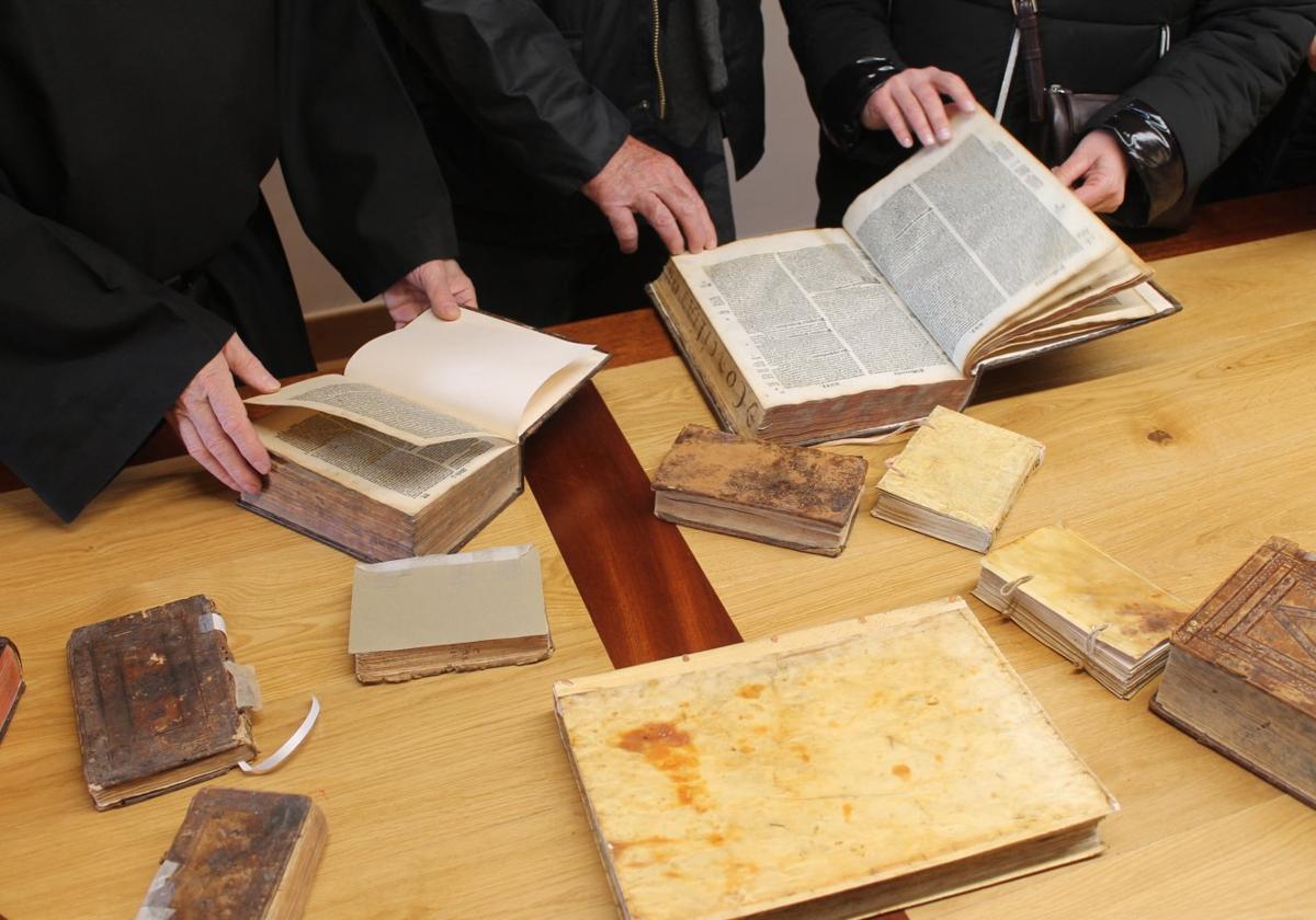 Varias personas hojean algunas de las obras recién salidas del taller que, arregladas, se reincorporarán a la biblioteca del monasterio..