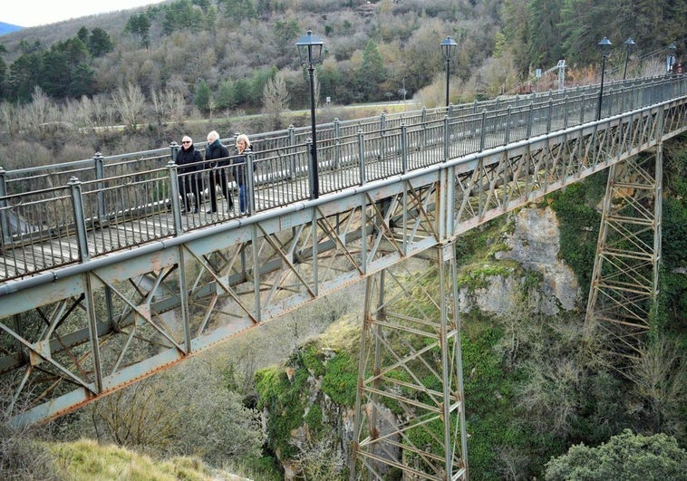 Tres vecinas del pueblo transitan este lunes por el deteriorado puente de hierro de Ortigosa de Cameros, que será rehabilitado.