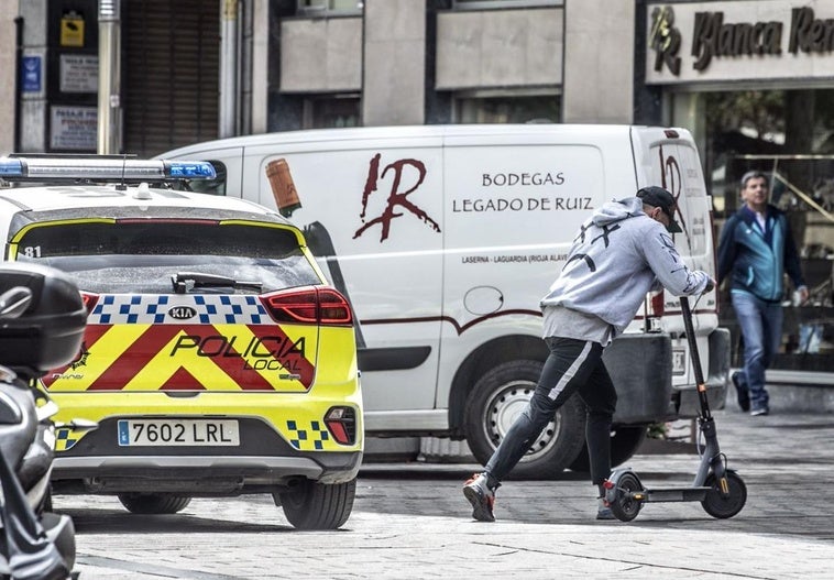 Un joven circula en patinete, al paso de un coche de la Policía Local.