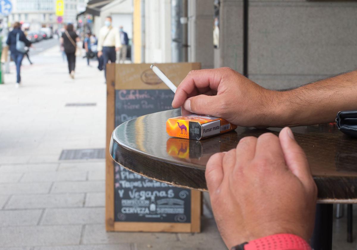 Una persona sostiene un cigarrillo en una terraza.