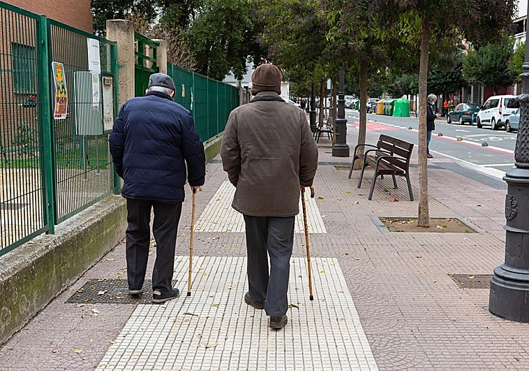 Dos personas mayores pasean por una calle de Logroño ayudadas por un bastón.