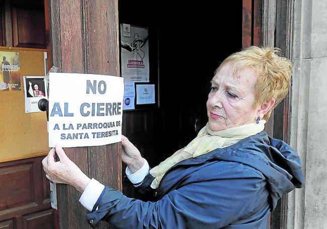 Una feligresa coloca un cartel de protesta en la puerta.