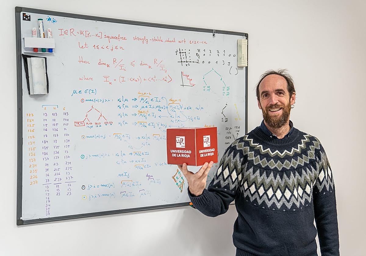 Eduardo Sáenz de Cabezón, delante de una pizarra repleta de fórmulas y sosteniendo el logo de la Universidad de La Rioja.