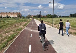 Un ciclista y dos peatones transitan por el carril ciclopeatonal urbanizado en medio del solar de Ramblasque.