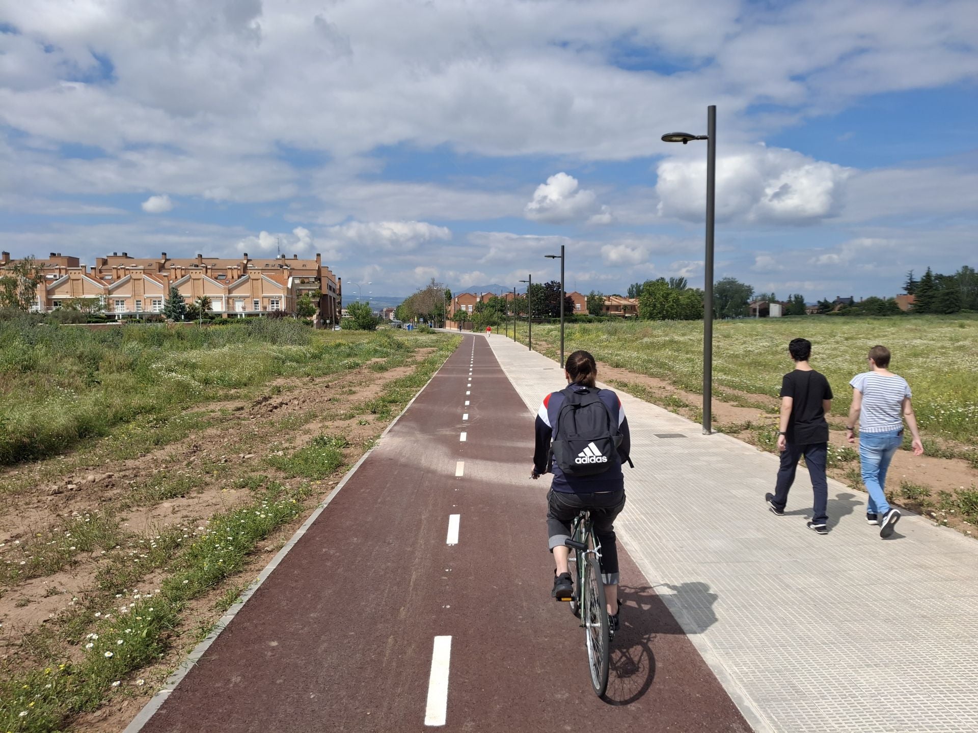 Un ciclista y dos peatones transitan por el carril ciclopeatonal urbanizado en medio del solar de Ramblasque.