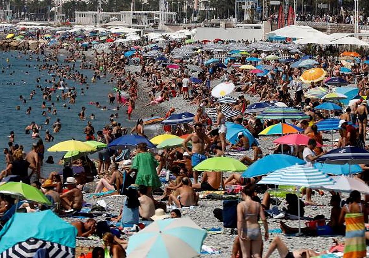 Una multitud bajo el sol en una playa, en la que muchos turistas, no obstante, se protegen bajo sombrillas.