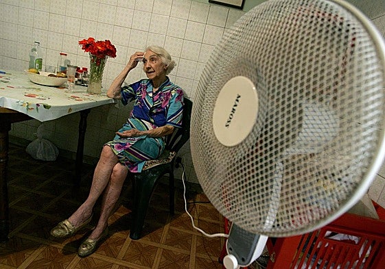 Una anciana trata de combatir el calor en el interior de su casa con un ventilador en un rincón de la cocina.