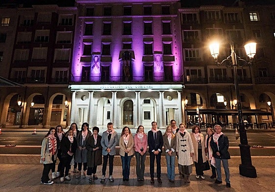 Varios representantes de la política riojana frente al edficio de la Delegación del Gobierno iluminado de rosa.