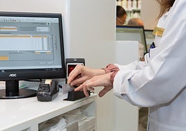 Una farmacéutica pasa por el lector la tarjeta sanitaria de un paciente para comprobar la medicación disponible en el sistema de receta electrónica.