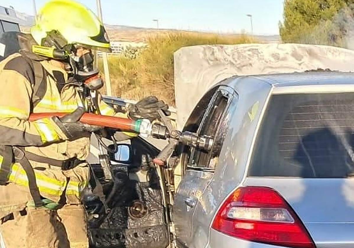 Un bombero sofoca las llamas de uno de los turismos.