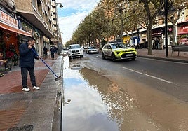 Un comerciante achica el agua de la acera junto a su tienda.