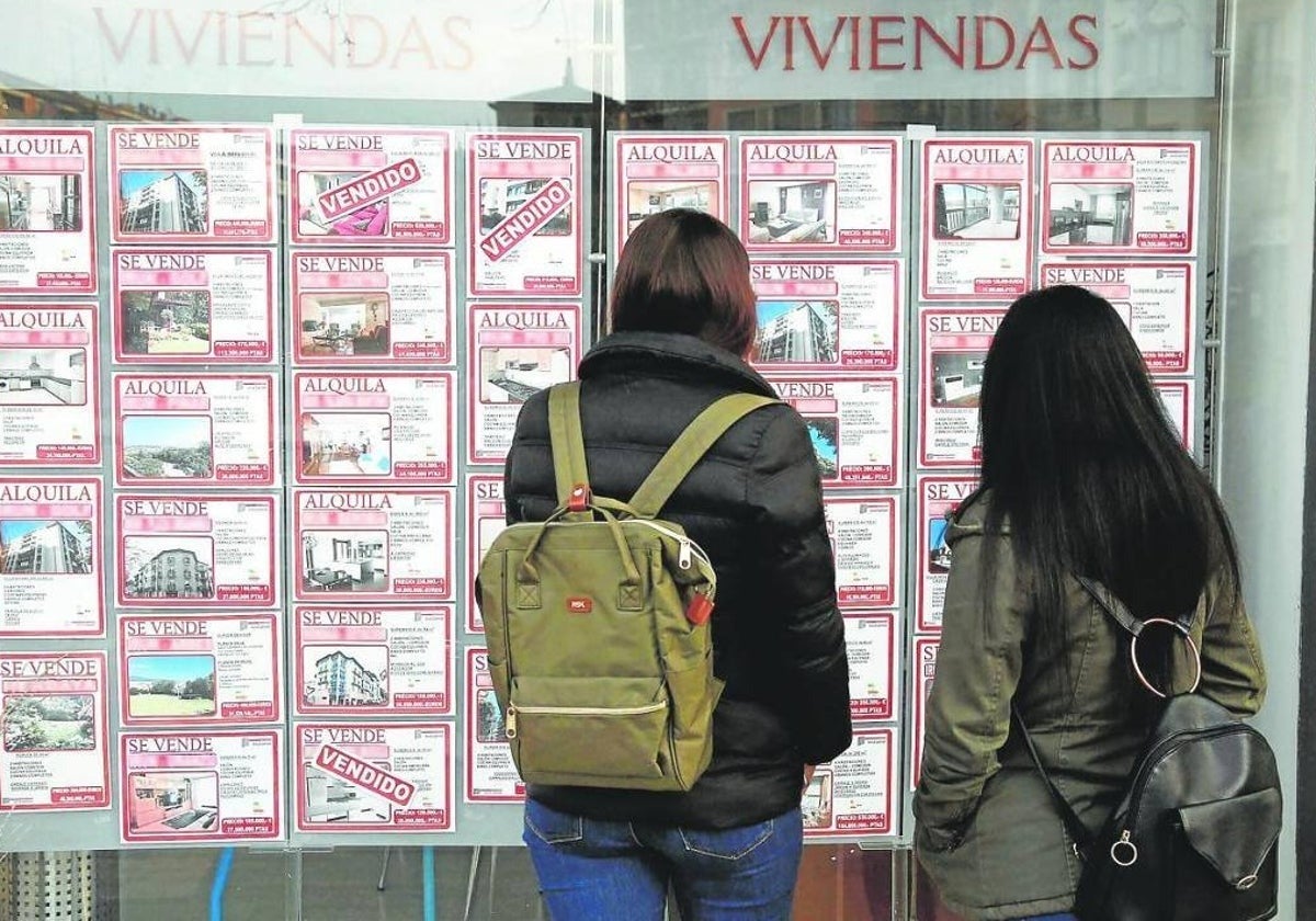 Dos mujeres miran los precios de los pisos en un escaparate.