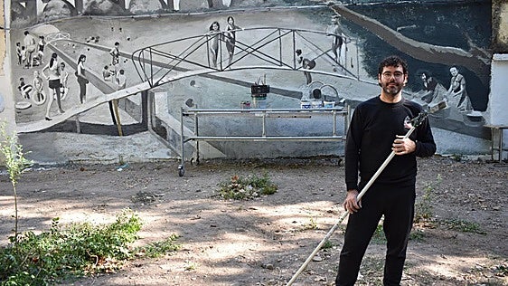 Miguel Ezquerro y, al fondo, la obra mural que ha realizado en Lodosa sobre las antiguas piscinas en el Ebro