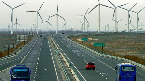 Varios vehículos por una carretera al lado de un parque eólico.