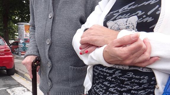 Una anciana paseando del brazo de su cuidadora.