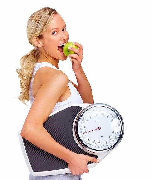 Una mujer se come una manzana mientras lleva una báscula. 