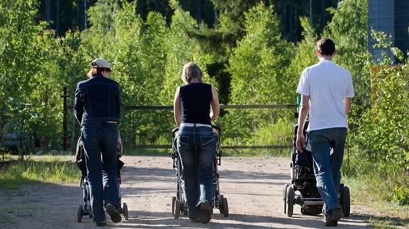 Tres padres pasean a sus hijos por el parque. 