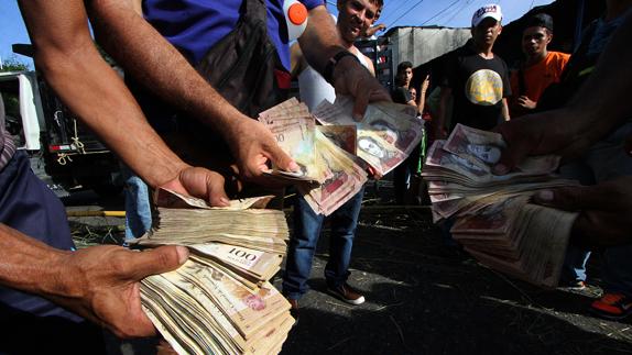 Varios hombres enseñan billetes de 100 bolívares mientras hacen fila en las inmediaciones del Banco Central de Venezuela.
