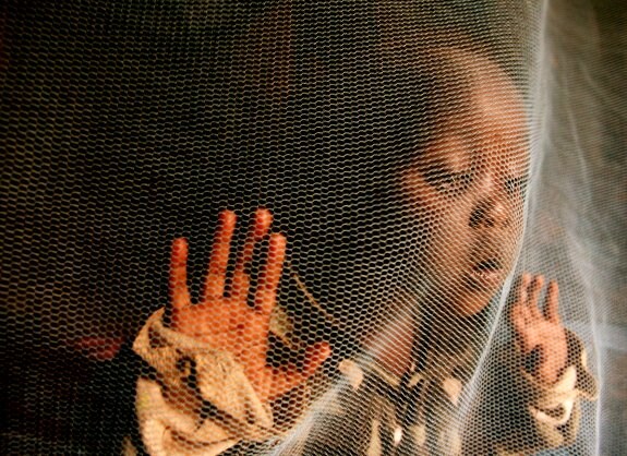 Una pequeña keniana con malaria juega detrás de una mosquitera. :: Stephen Morrison / efe