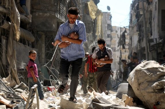 Dos hombres caminan entre los escombros con sendos bebés en brazos tras un ataque aéreo en la ciudad siria de Alepo. :: AMEER ALHALBI/afp
