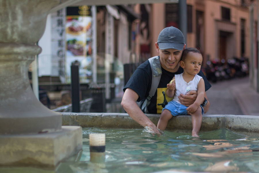 Un papá refresca los pies a su hijo en una fuente 