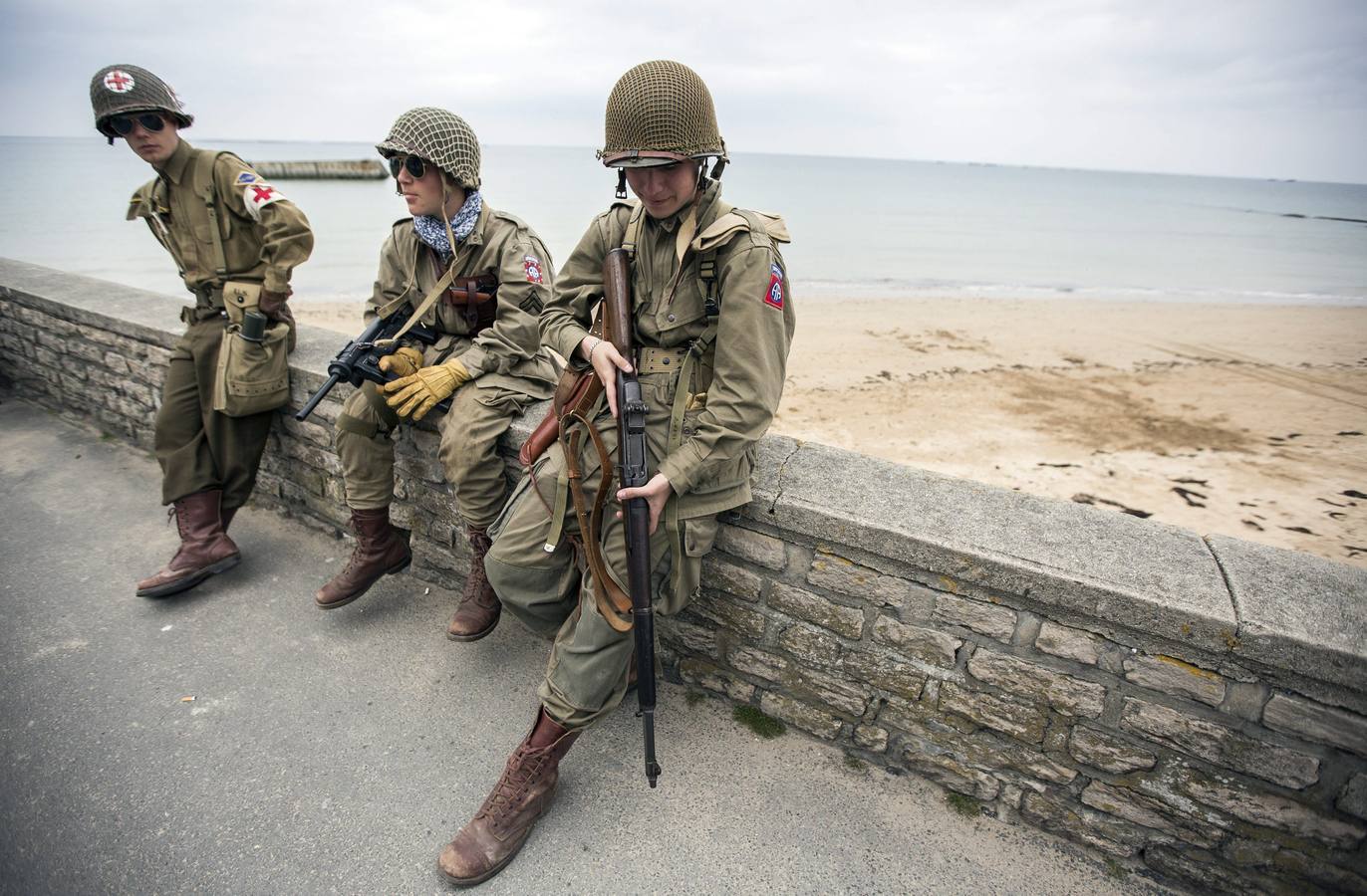 Varios entusiastas de la Segunda Guerra Mundial, con réplicas de los uniformes militares de la época, se sientan en un muro en la costa de Arromanches, en Normandía.