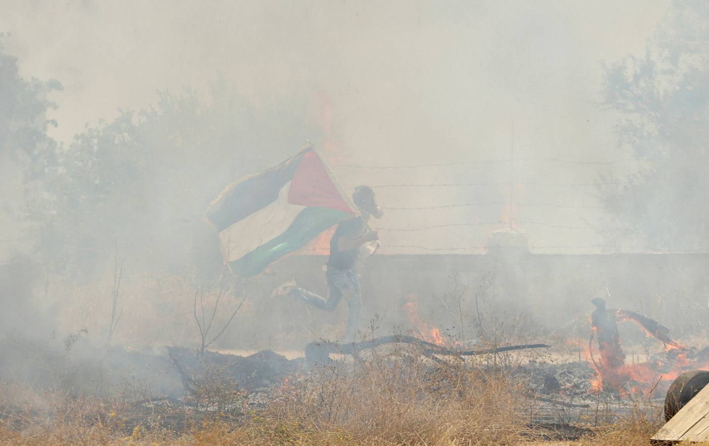 Un manifestante con una bandera palestina corre envuelto por el gas lanzado por las tropas israelíes en Bilin, en la franja de Gaza, cerca de Ramala.