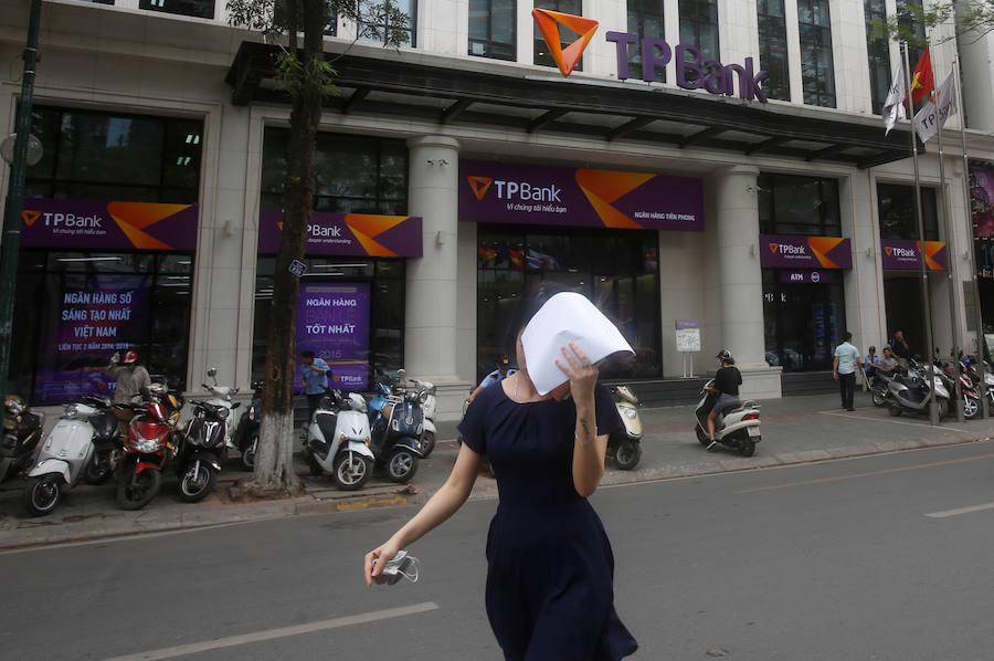 Una mujer cubre su cara mientras sale el banco Tien Phong en Hanoi.