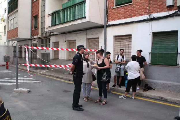 Varios vecinos que han desalojado sus pisos en el grupo Antonio Catalá y propietarias esperan en la calle junto a un agente de la Policía Local. 